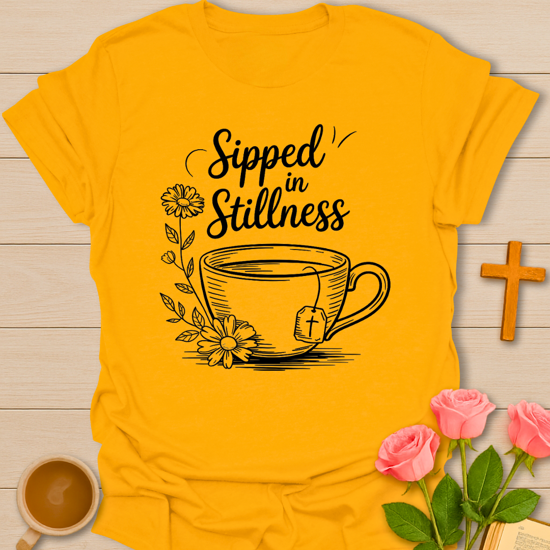 Gold Christian t-shirt design featuring a teacup with a cross tea tag, floral elements, and the phrase “Sipped in Stillness” symbolizing faith and quiet reflection