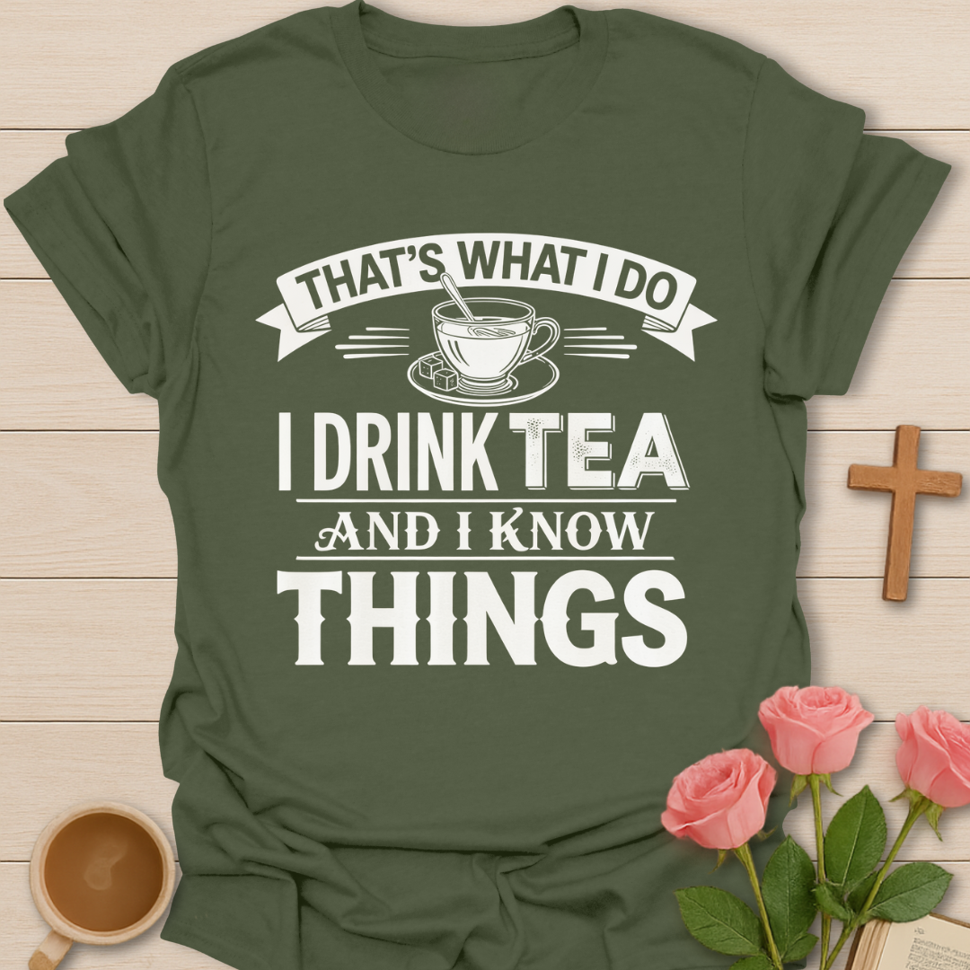 Green t-shirt with tea-themed graphic and text on a wooden surface with flowers and a cross.