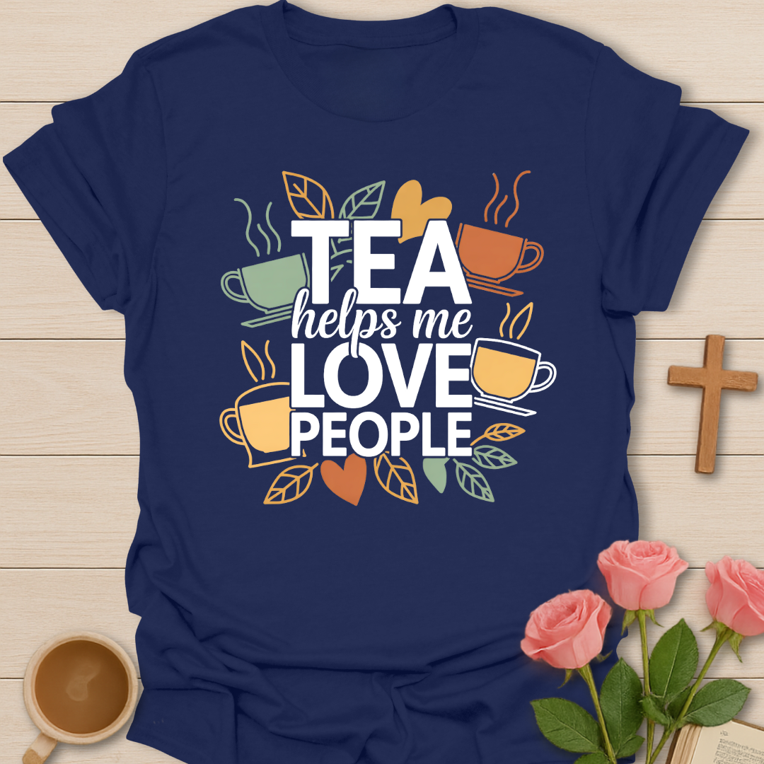 Navy blue t-shirt with illustrated tea cups and leaves surrounding the phrase “Tea Helps Me Love People” in warm earthy tones on a dark background.