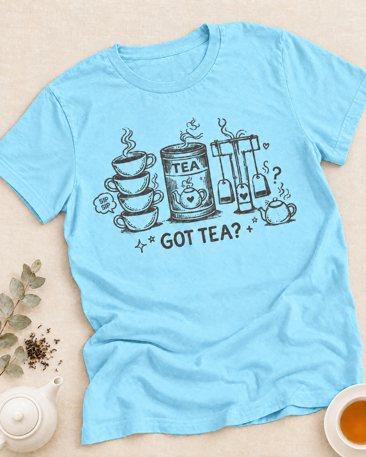 Smiling woman in a Got Tea graphic T-shirt holding a mug in a warm, cozy room with teapot, flowers, and Tea Lover Lifestyle collection text above.