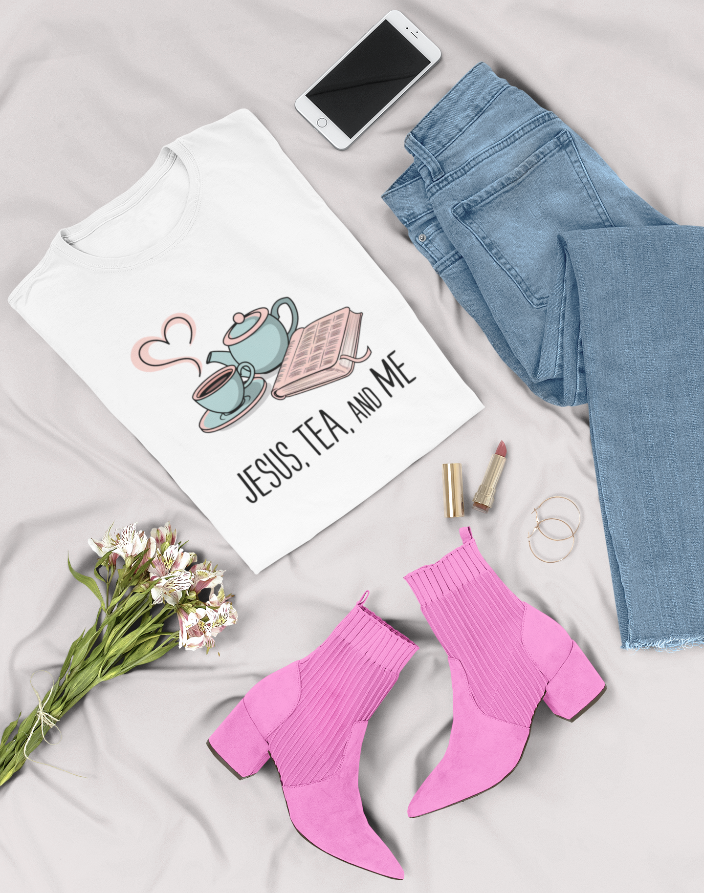 Jesus Tea and Me t-shirt on a bed with daisies, pink boots, jeans, cell phone, lip sticks and earrings