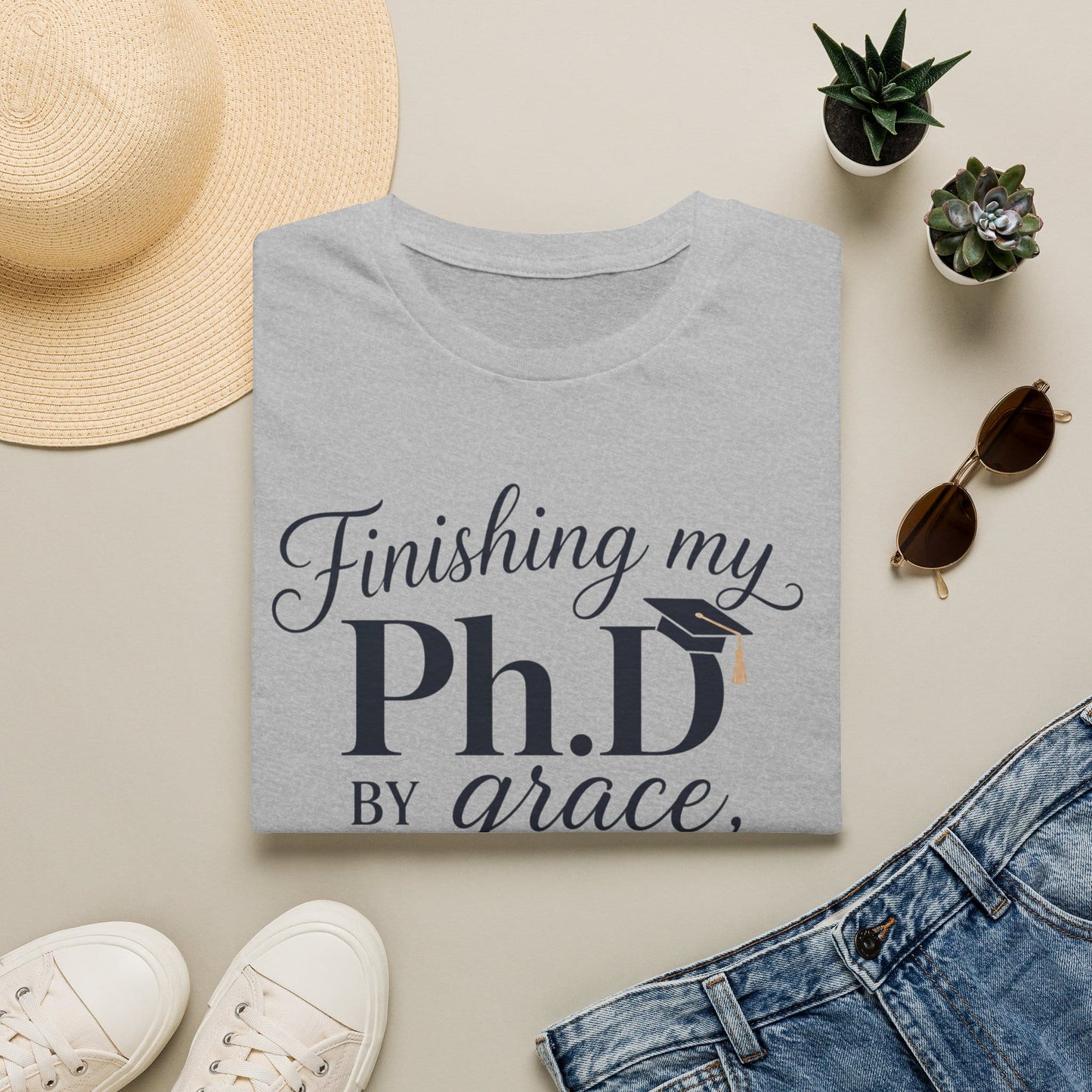 PhD By Grace shirt with large navy PhD lettering, graduation cap, script grace text, sleepless nights phrase, and teacup illustration.