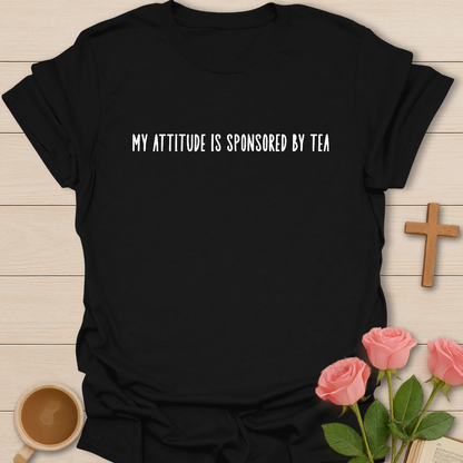 Black t-shirt with 'My attitude is sponsored by tea' text on a wooden surface with a cup of coffee and roses.