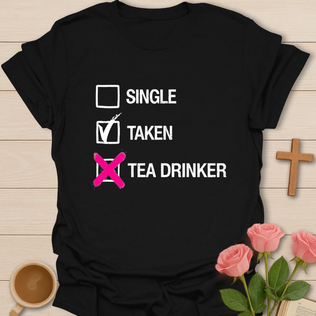 Black t-shirt with text 'Single, Taken, Tea Drinker' on a wooden surface with flowers and a cup.