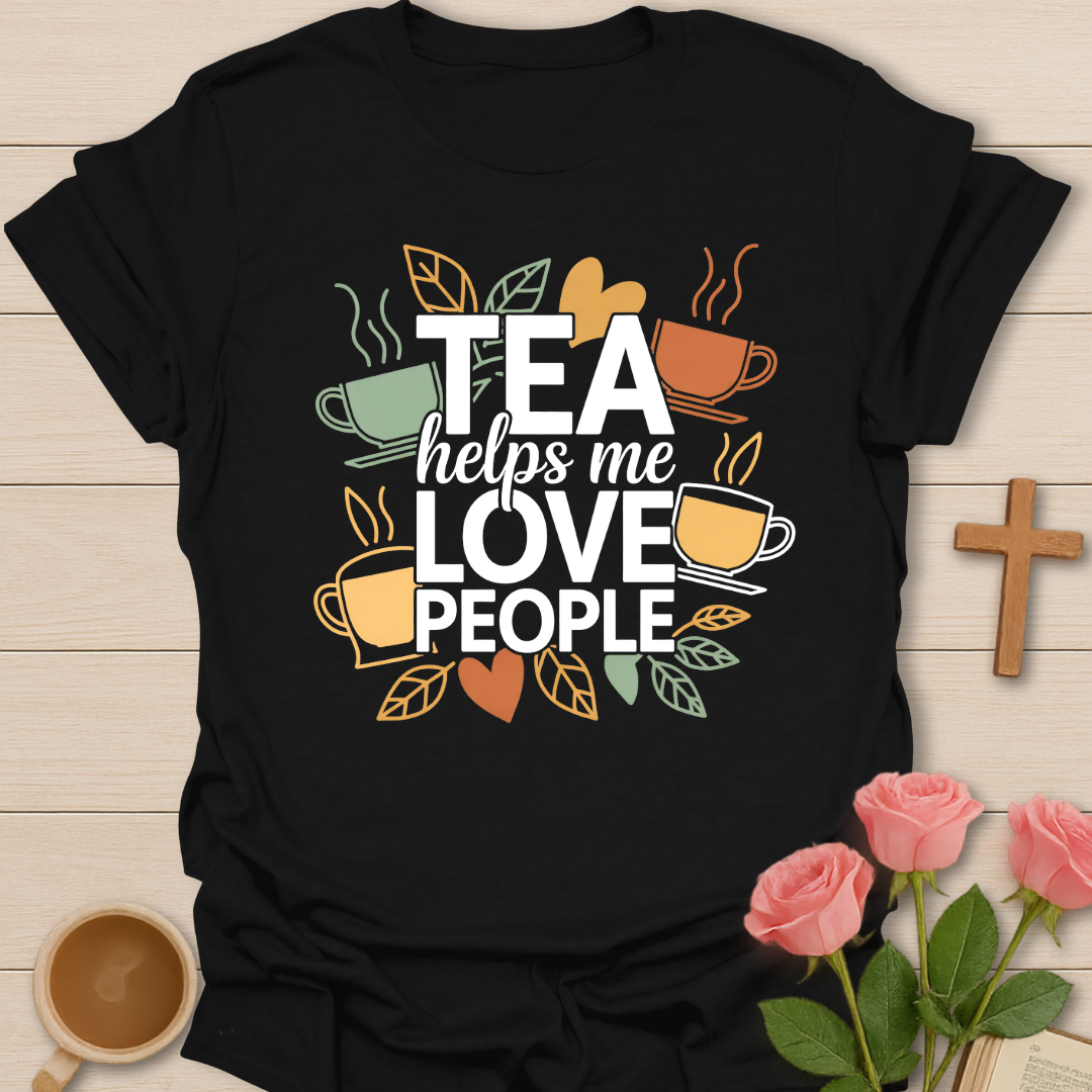 Black t-shirt with illustrated tea cups and leaves surrounding the phrase “Tea Helps Me Love People” in warm earthy tones on a dark background.