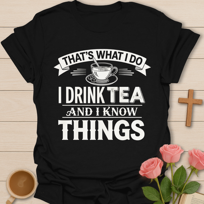 Black t-shirt with 'I Drink Tea and I Know Things' text on a wooden surface with a cup of tea and roses.