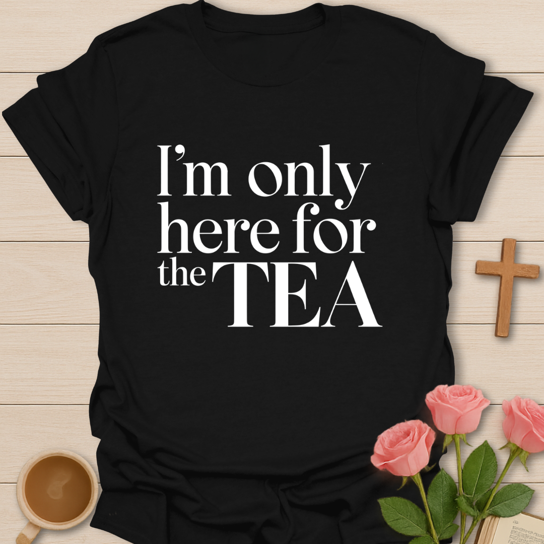 Black t-shirt with 'I'm only here for the TEA' text on a wooden surface with flowers and a cup.
