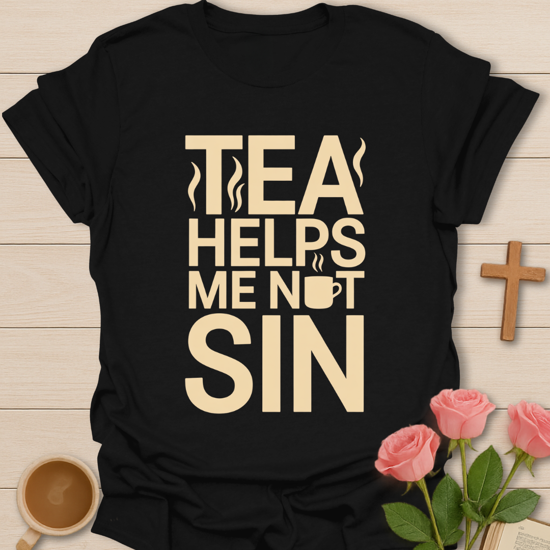 Black t-shirt with 'Tea Helps Me Not Sin' text on a wooden surface with flowers and a cup.