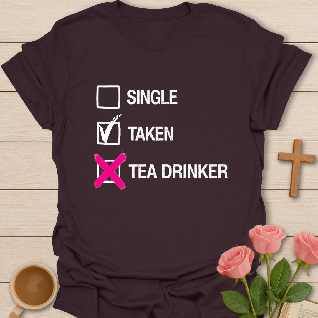 Brown t-shirt with text 'Single, Taken, Tea Drinker' on a wooden surface with flowers and a cup.