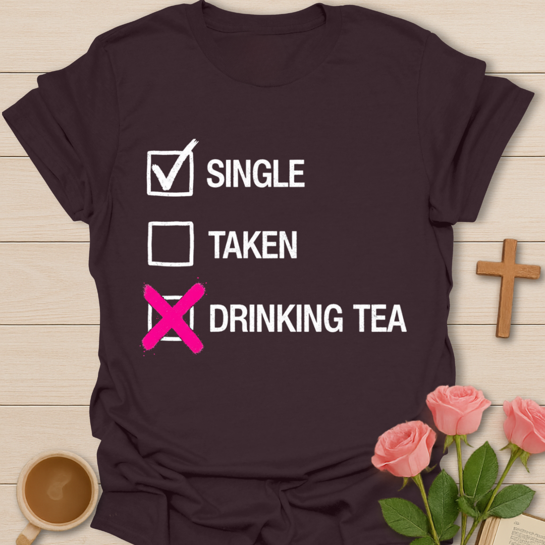 Brown t-shirt with humorous text design on a wooden surface with flowers and a cup.