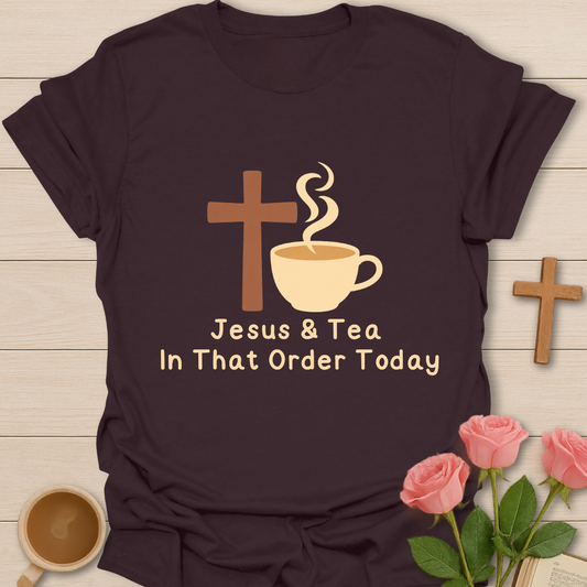 Dark t-shirt with 'Jesus & Tea In That Order Today' design on a wooden surface with a cup of tea and roses.