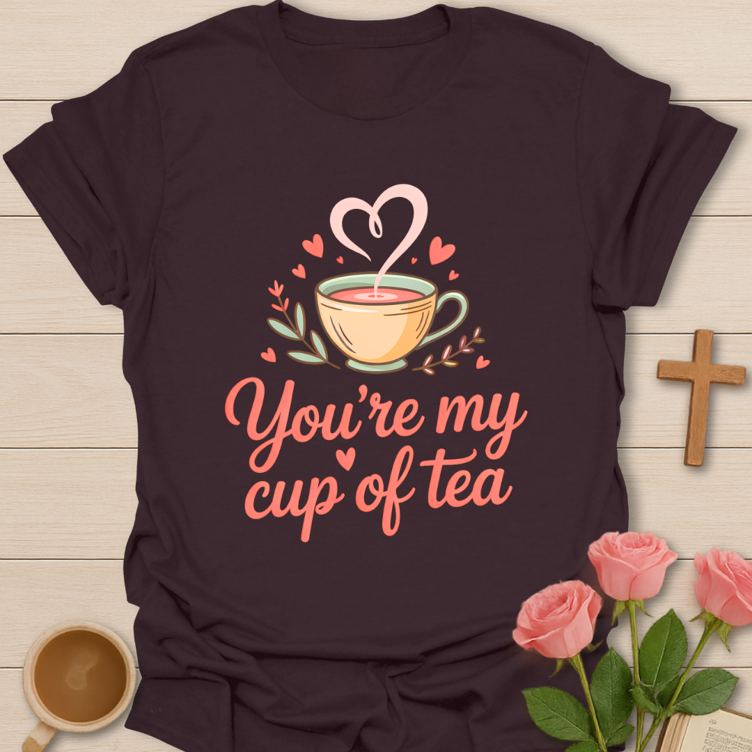 Brown t-shirt with a graphic of a teacup and text 'You're my cup of tea' on a wooden surface with flowers and a mug.