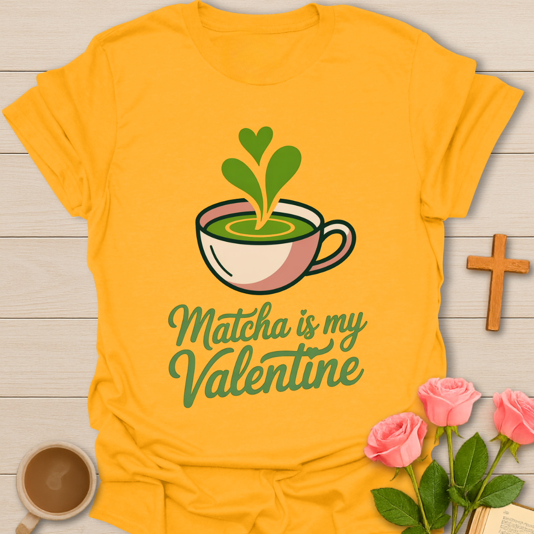 Yellow t-shirt with matcha-themed design and text on a wooden surface with flowers and a cross.