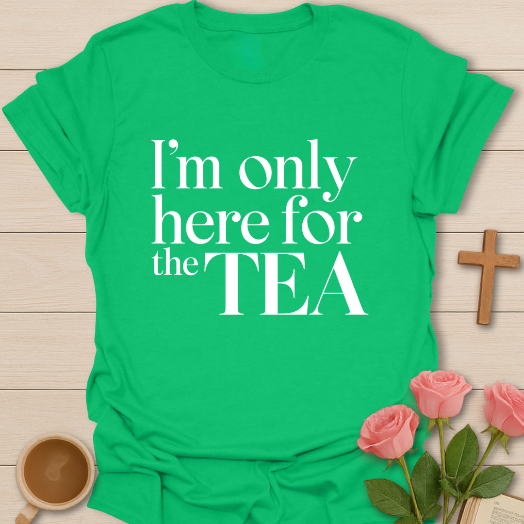 Green t-shirt with 'I'm only here for the TEA' text on a wooden surface with flowers and a cup.