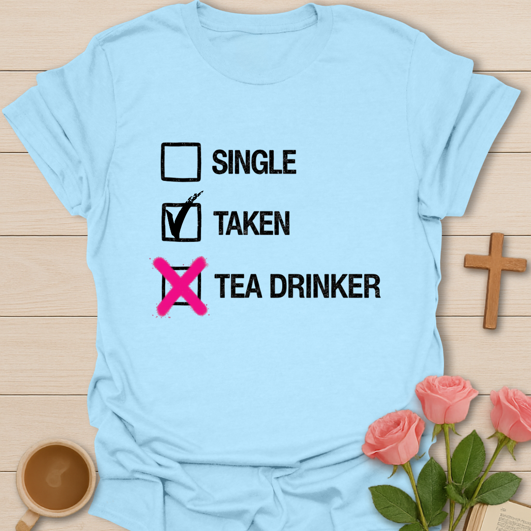 Light blue t-shirt with humorous text design on a wooden surface with flowers and a cross.