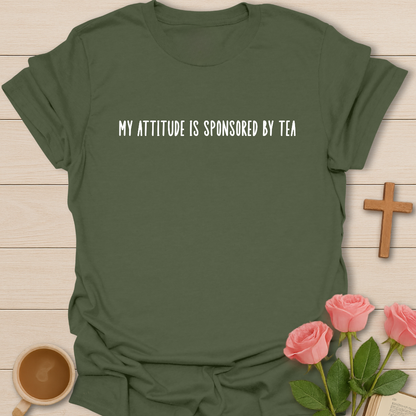 Green t-shirt with 'My attitude is sponsored by tea' text on a wooden surface with a cup of coffee and roses.