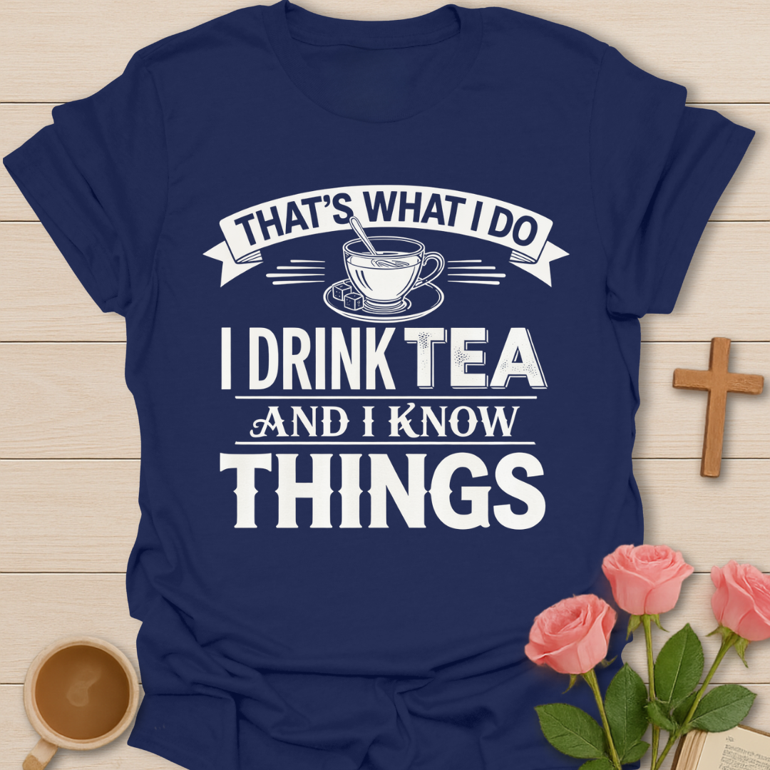 Navy blue t-shirt with white text and graphics on a wooden surface with flowers and a mug.