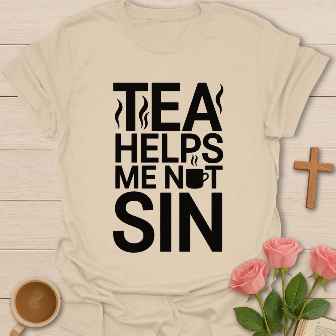 Beige t-shirt with black text 'TEA HELPS ME NOT SIN' on a wooden surface with a cup of tea and roses.