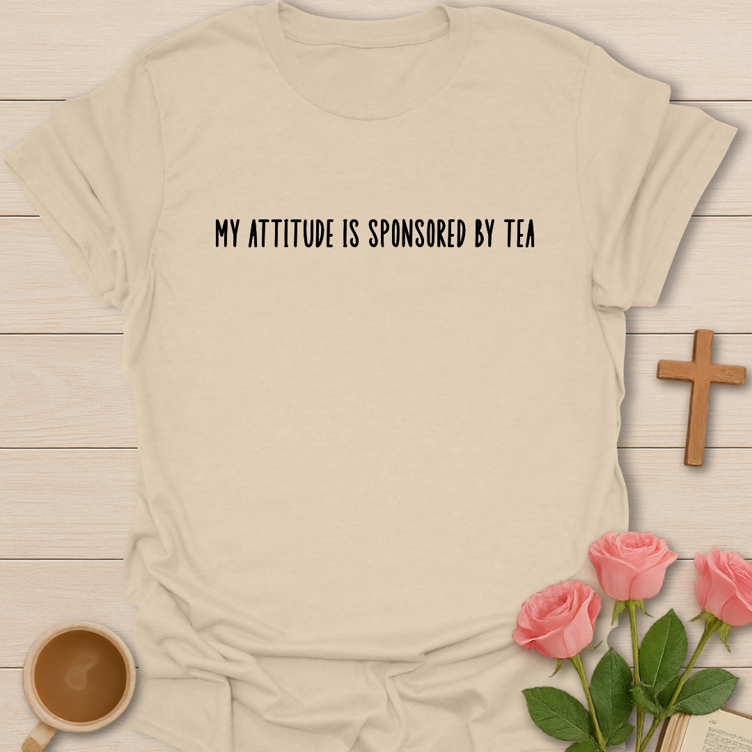 Beige t-shirt with 'My attitude is sponsored by tea' text, coffee cup, and pink roses on a wooden surface.