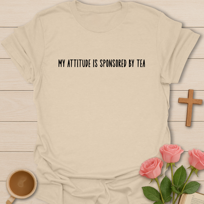 Beige t-shirt with 'My attitude is sponsored by tea' text, coffee cup, and pink roses on a wooden surface.