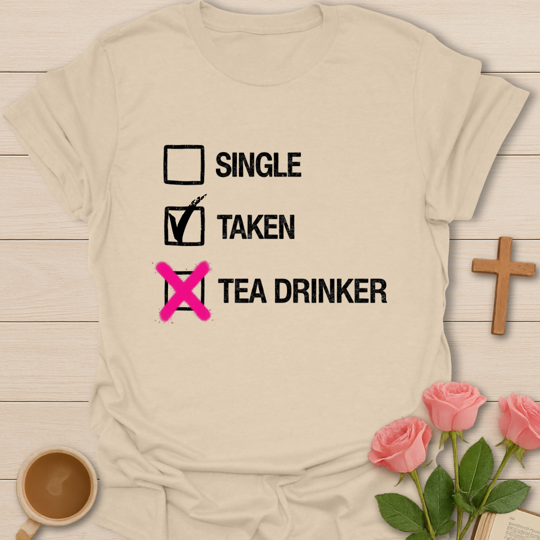Beige t-shirt with humorous checkboxes design on a wooden surface with flowers and a cup of coffee.