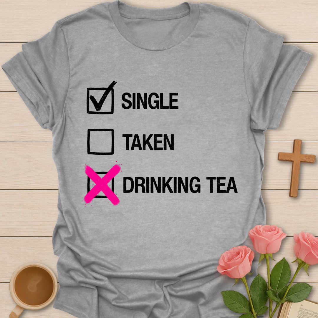 Gray t-shirt with humorous text design on a wooden surface with flowers and a cup.
