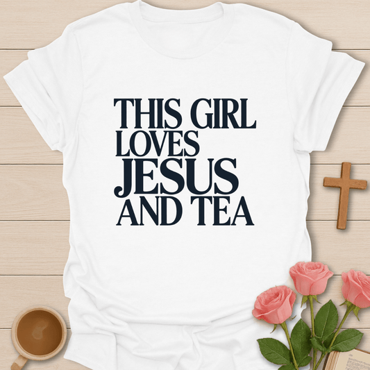 White t-shirt with 'This Girl Loves Jesus and Tea' text on a wooden surface with flowers and a cross.