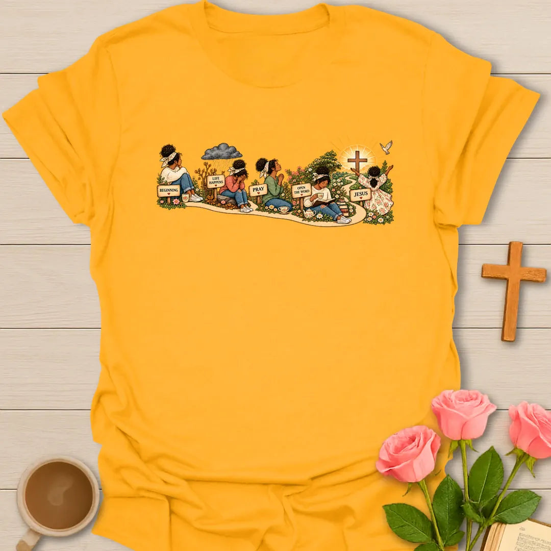 Faith Story t-shirt showing a woman's journey along a path with signs reading Beginning, Life Happens, Pray, Open The Word and Jesus, ending at a cross in a sunrise - Gold