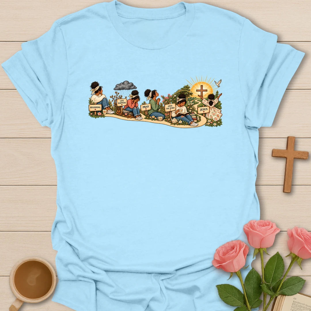 Faith Story t-shirt showing a woman's journey along a path with signs reading Beginning, Life Happens, Pray, Open The Word and Jesus, ending at a cross in a sunrise - Light Blue
