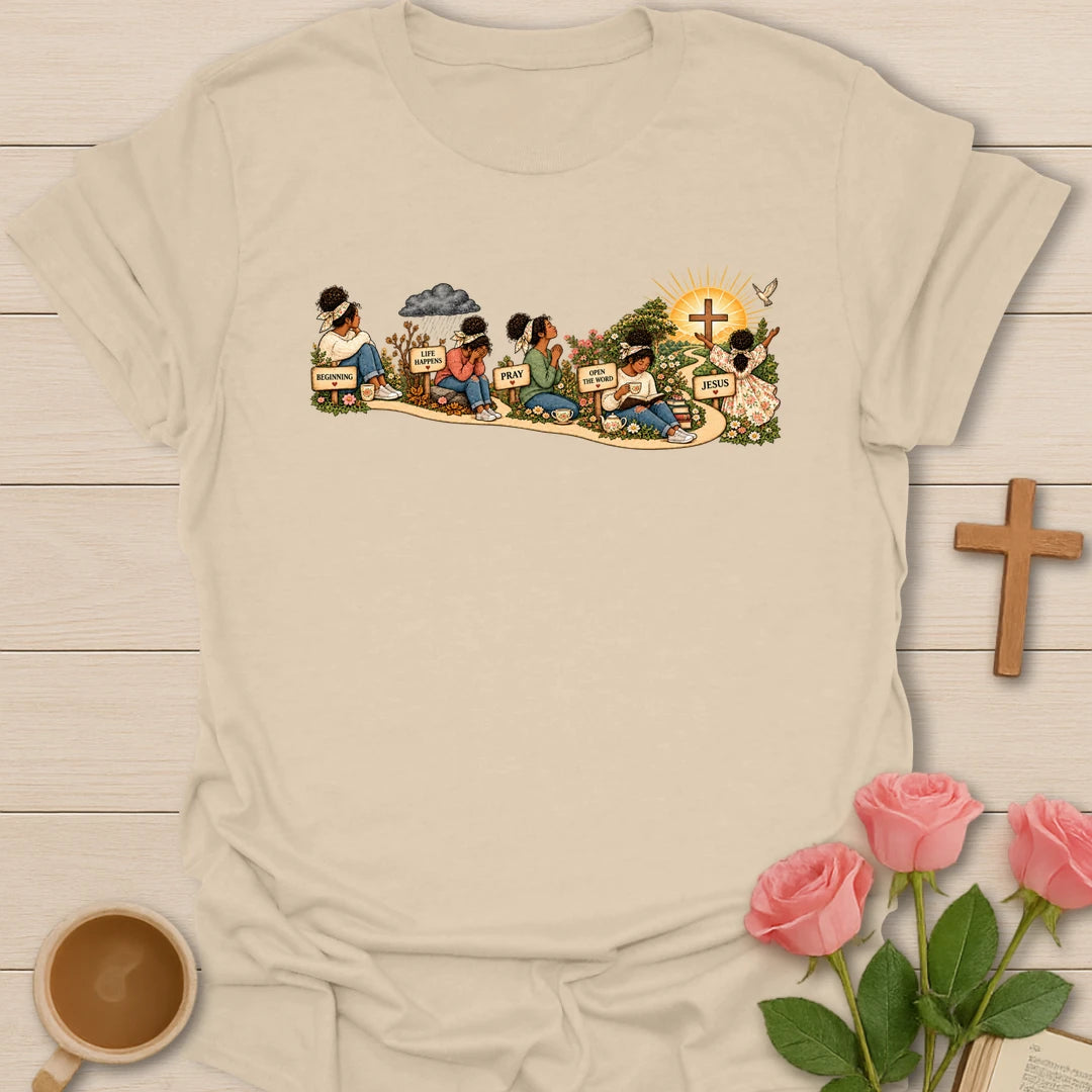 Faith Story t-shirt showing a woman's journey along a path with signs reading Beginning, Life Happens, Pray, Open The Word and Jesus, ending at a cross in a sunrise - Sand