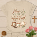 Low Caffeine High Faith t-shirt with script and vintage lettering, a hojicha tea tin, teacup, teapot and a cross made of tea leaves. - Sand