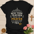 New York Teacher Runs On Prayer shirt with skyline, praying hands, distressed cream lettering, gold prayer text, and small teacup. - Black