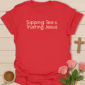 Sipping Tea and Trusting Jesus shirt with minimal cream typography on black background style. - Red