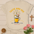 Taste And See tea shirt with steaming mug, marshmallow, cinnamon stick, cross, and sunburst. - Sand